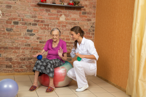 Senior Woman Sitting On A Gym Ball And Doing Exercise With Physical Therapist