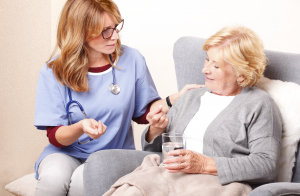 Portrait of senior patien sitting at home with home care nurse and giving medication to an elderly woman.