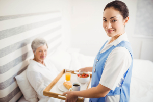 Portrait of nurse giving breakfast to senior women in bedroom